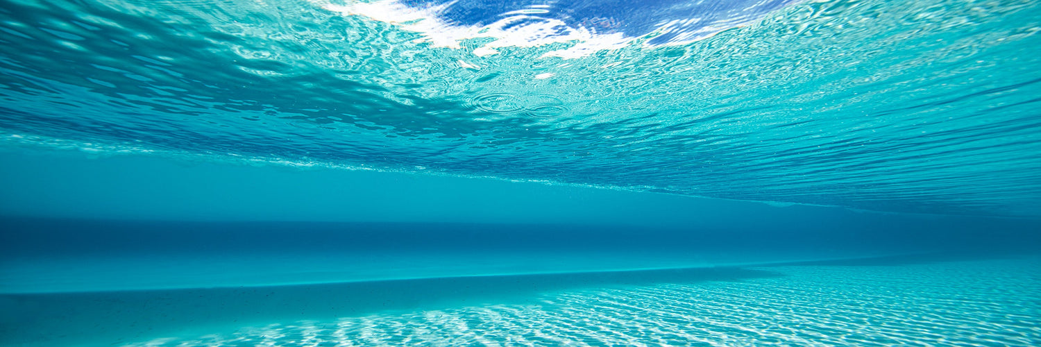 Underwater view of clear turquoise ocean with sunlight rippling across the sandy seabed