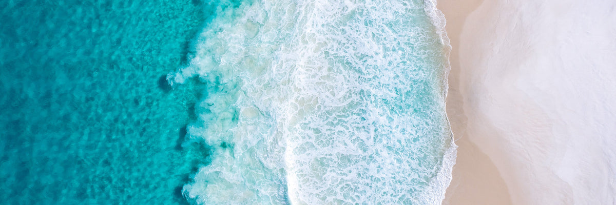 Aerial view of turquoise ocean waves meeting a white sandy beach
