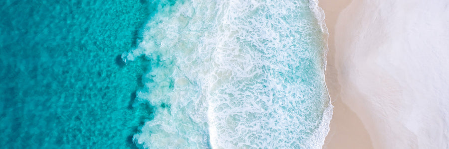Aerial view of turquoise ocean waves meeting a white sandy beach
