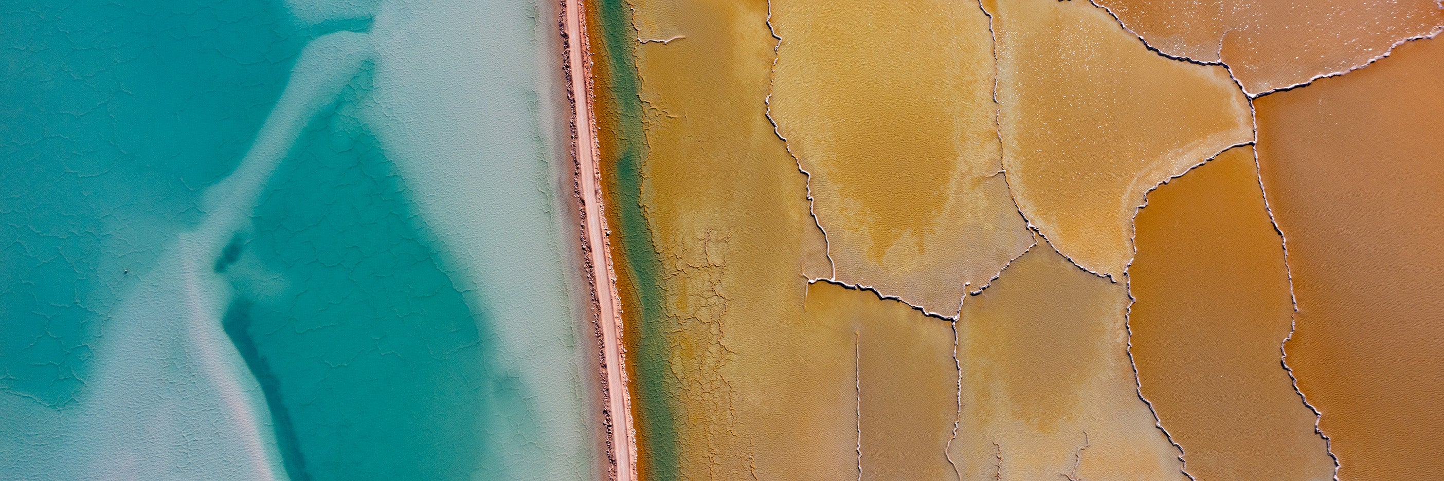 Aerial view of turquoise salt lake beside cracked golden salt flats